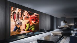 A photograph of a modern, grey living room with a large television screen as the focal point.